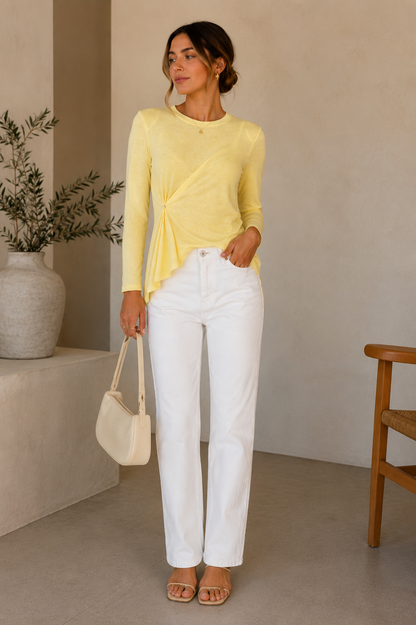Woman wearing a yellow top and white pants, holding a beige handbag indoors.