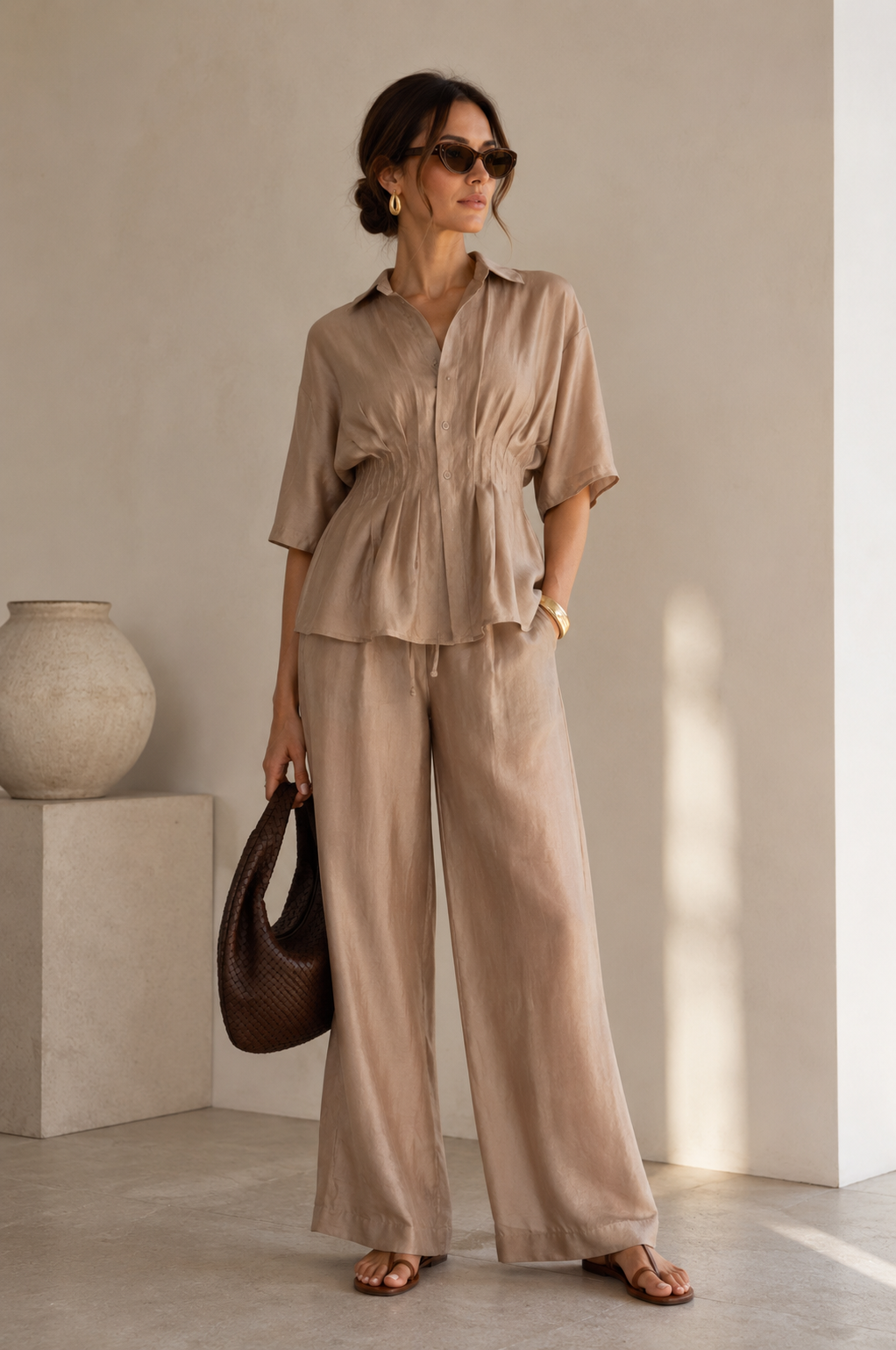 Woman in a beige outfit holding a brown bag indoors.