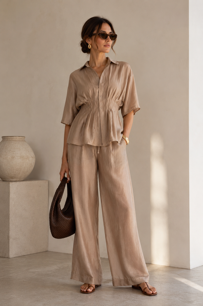 Woman in a beige outfit holding a brown bag indoors.