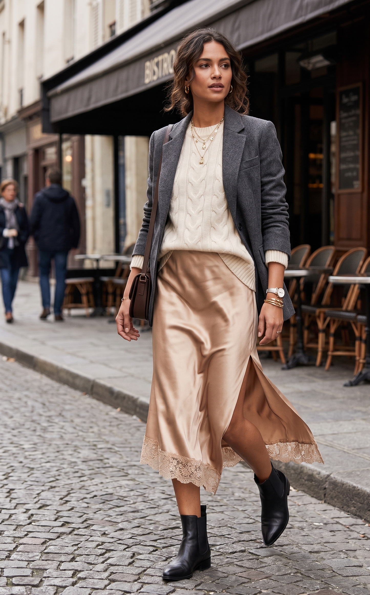 Woman walking on a street wearing a stylish outfit with a blazer, sweater, and skirt.