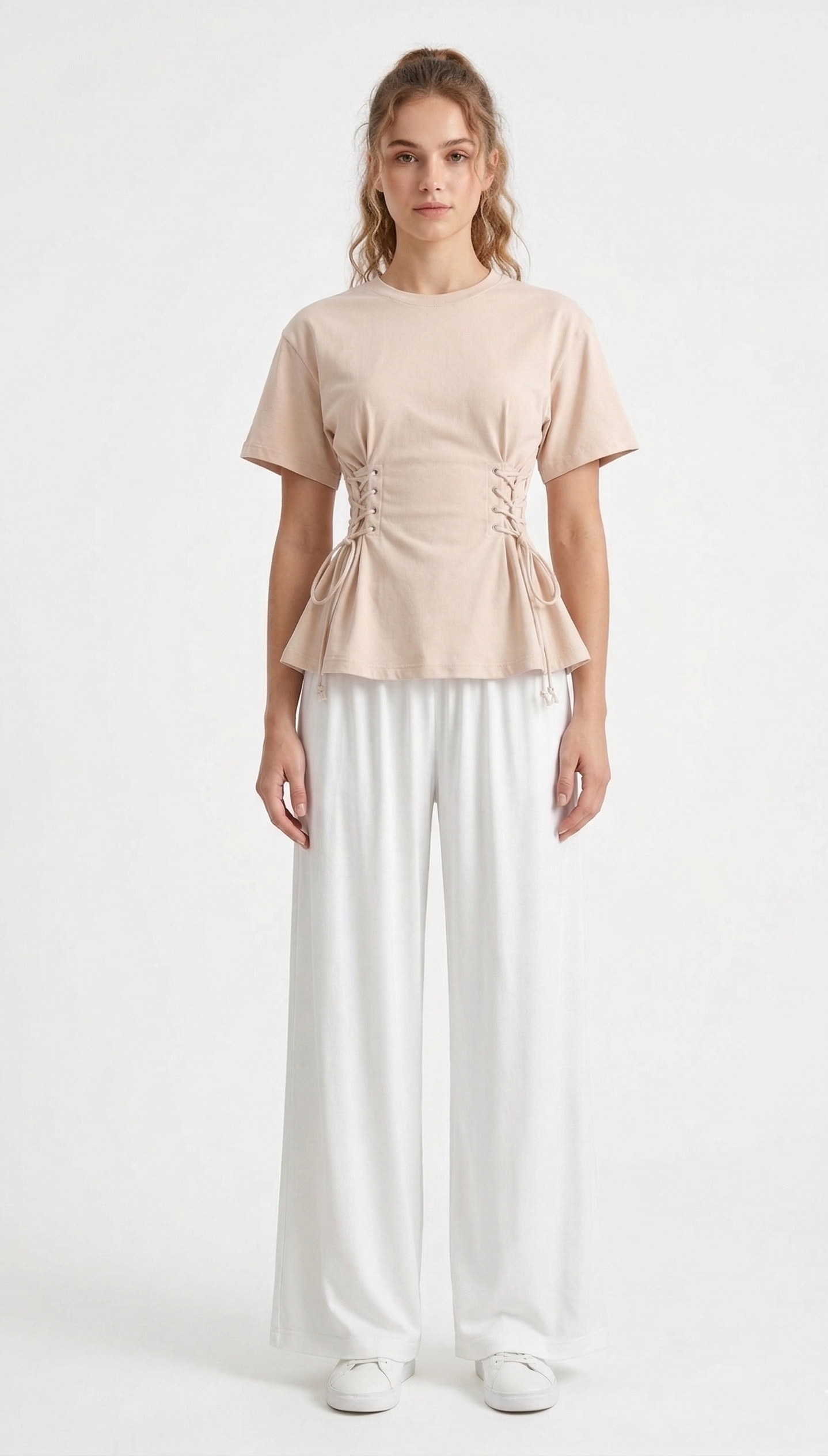 Woman wearing a beige top and white pants on a white background