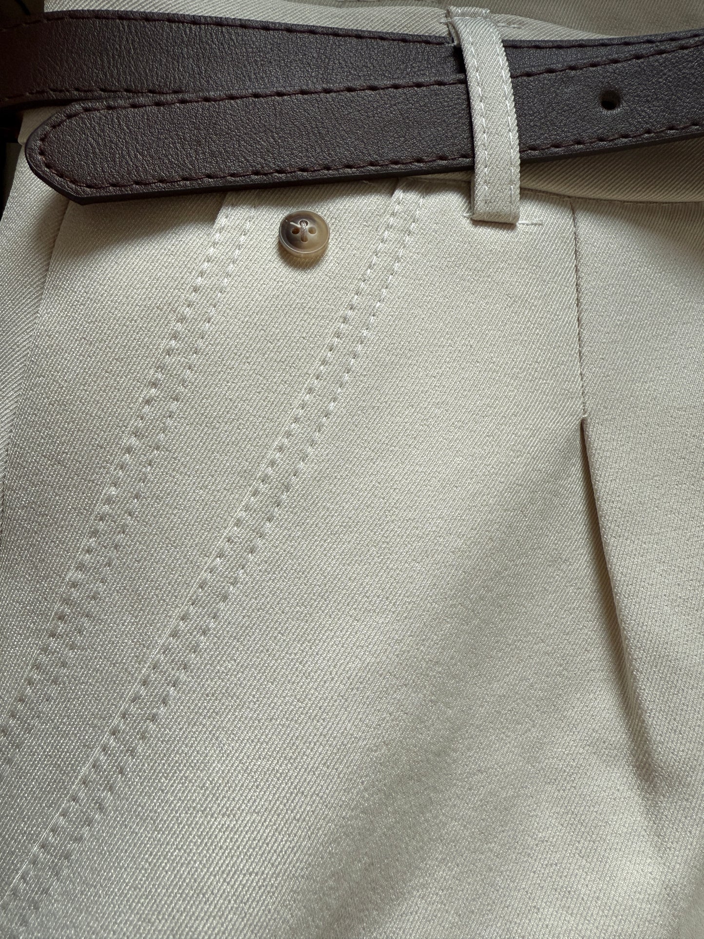 Close-up of beige pants with a button and gray belt