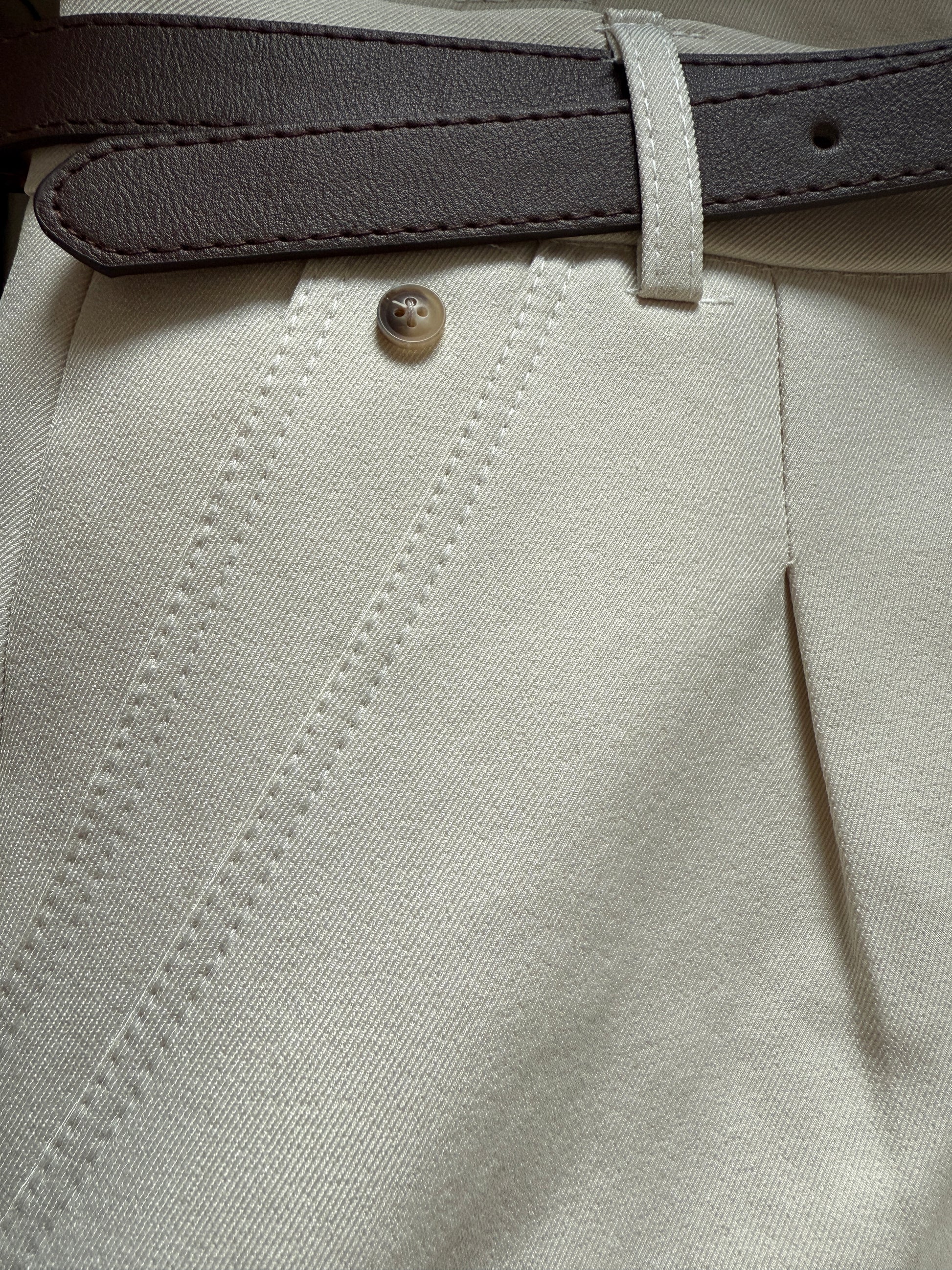 Close-up of beige pants with a button and gray belt