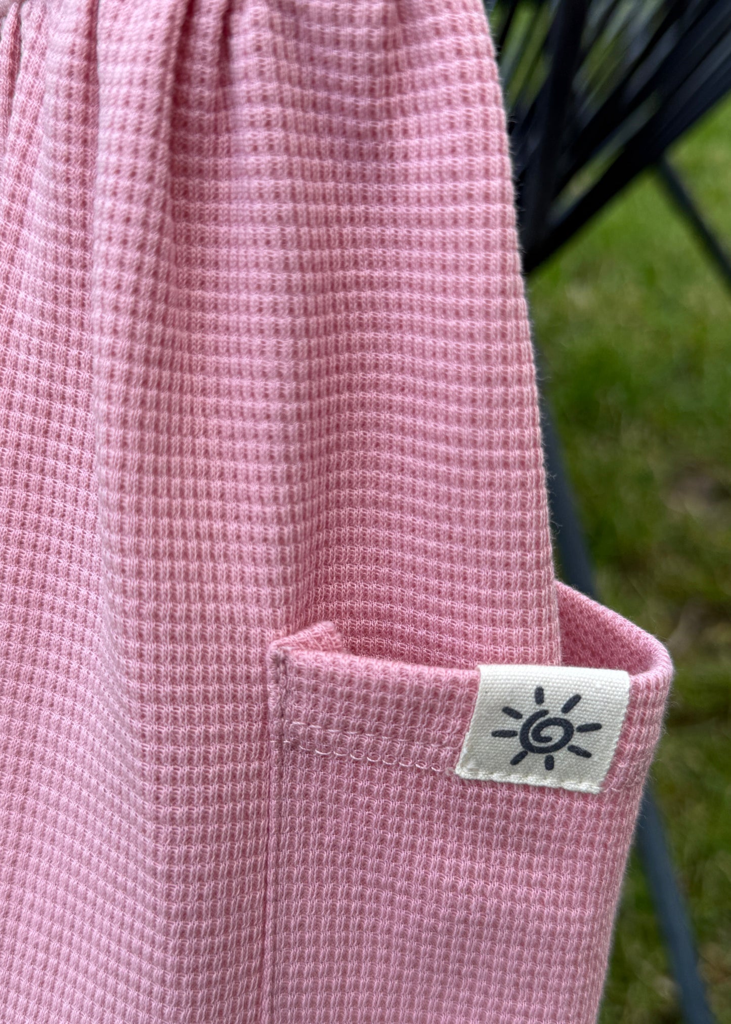 Pink textured fabric with a sun logo tag on a blurred green background