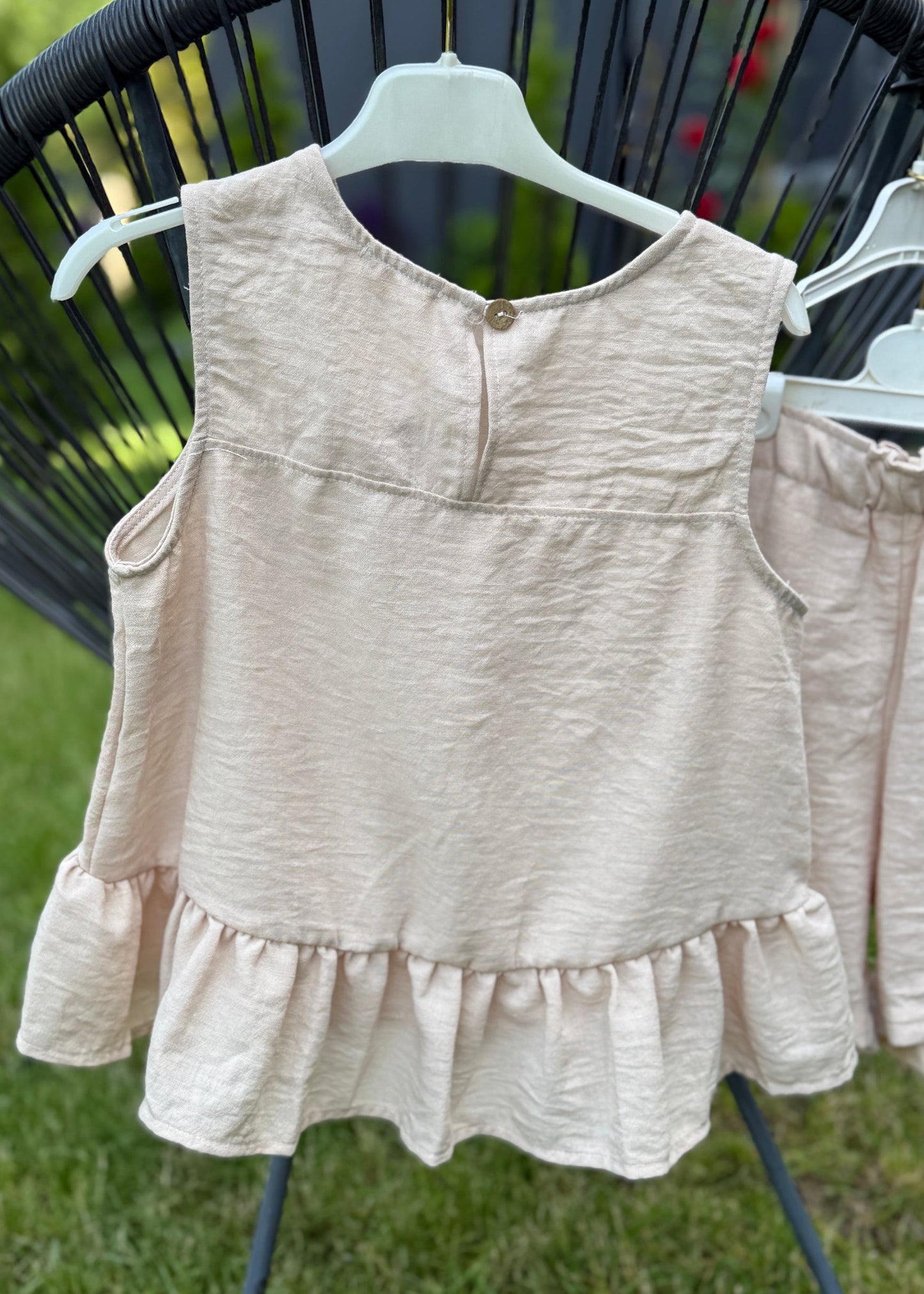 Beige sleeveless top and shorts on a hanger against a grassy background