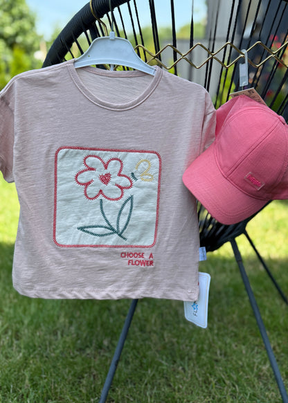 Children's t-shirt with flower design and pink cap on a stand outdoors