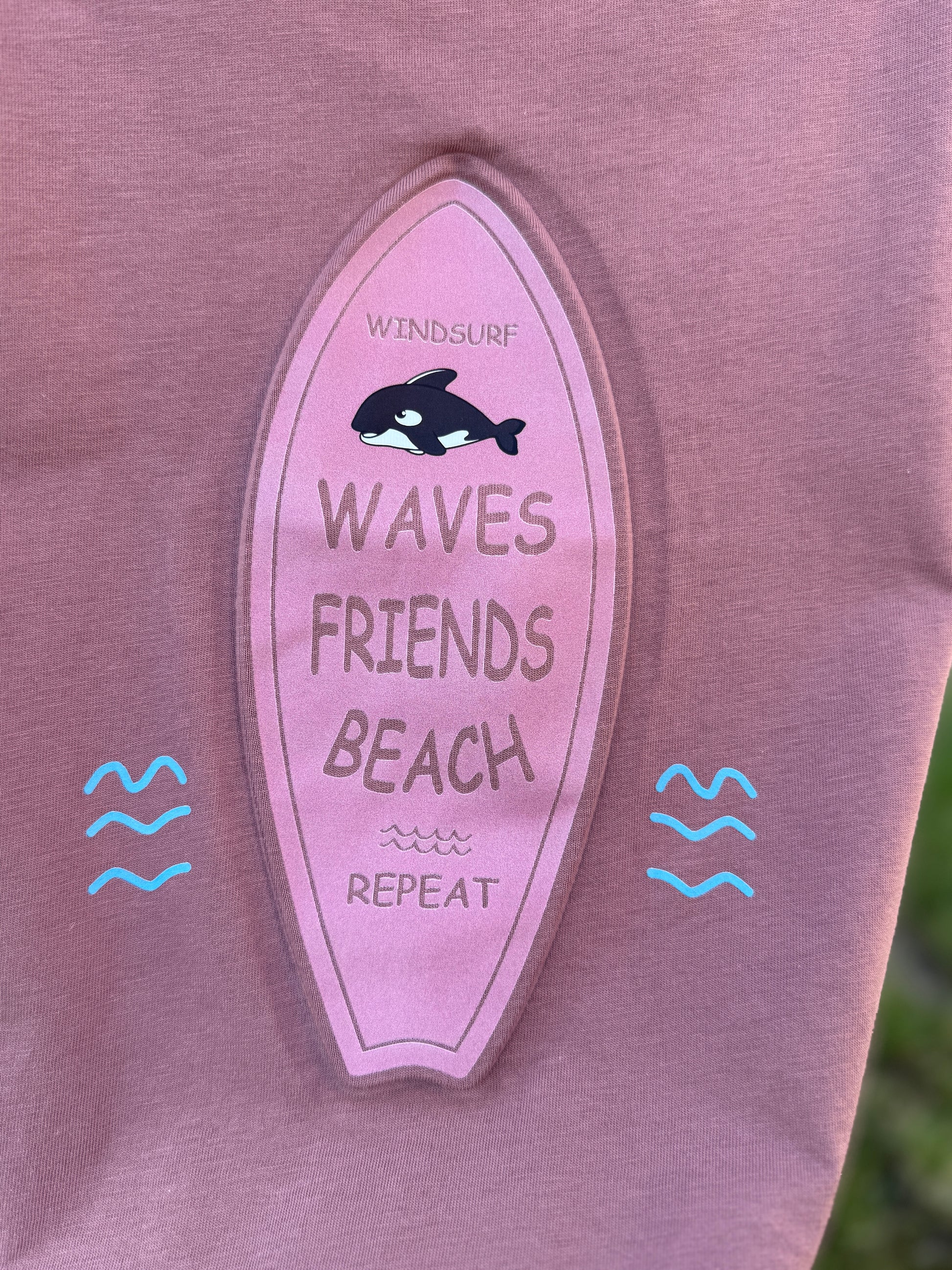 Pink surfboard-shaped patch with text and an orca design on a purple shirt.