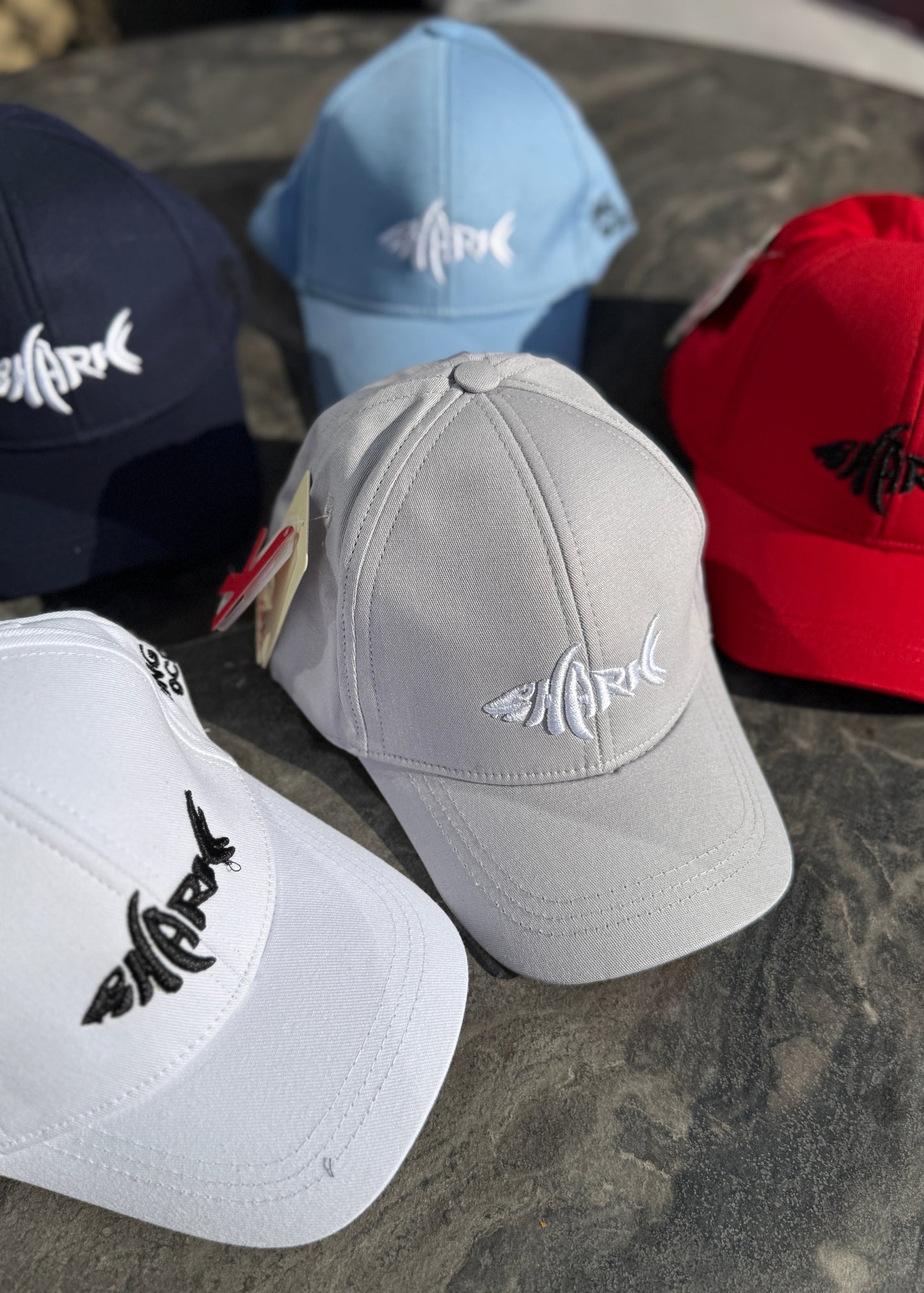 Five baseball caps in different colors with a brand logo on a stone surface.