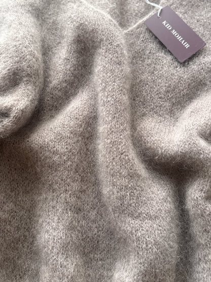 Close-up of a soft, fuzzy knit sweater in a light taupe-gray color, with a dark mauve brand tag reading 'KID MOHLIR' attached near the top right.