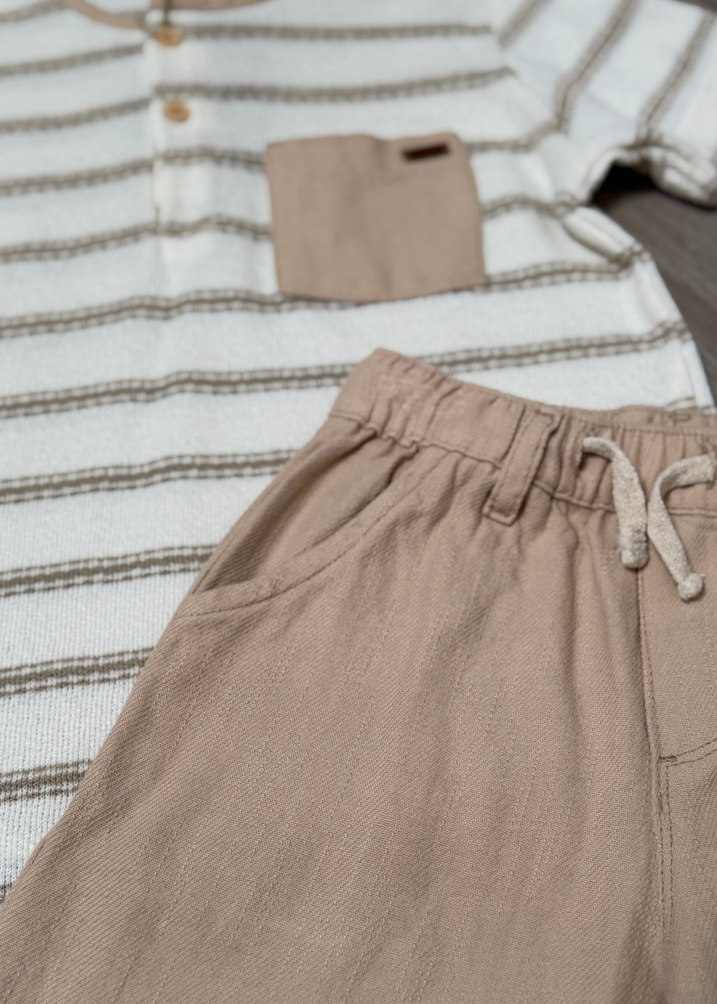 Beige pants with a striped shirt on a wooden surface