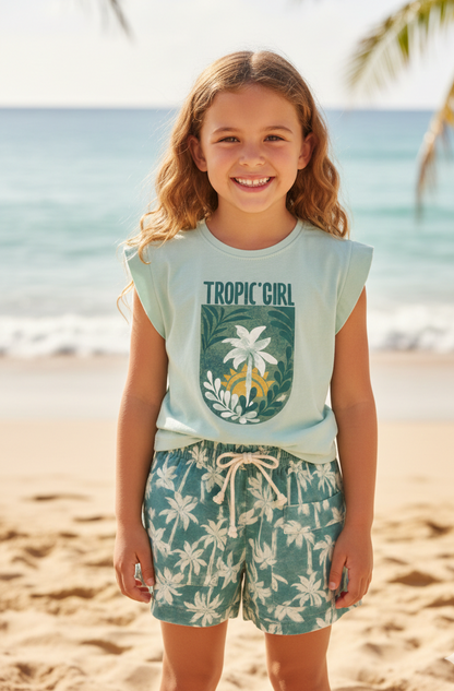 Young girl on a beach wearing a 'Tropic Girl' t-shirt and floral shorts.