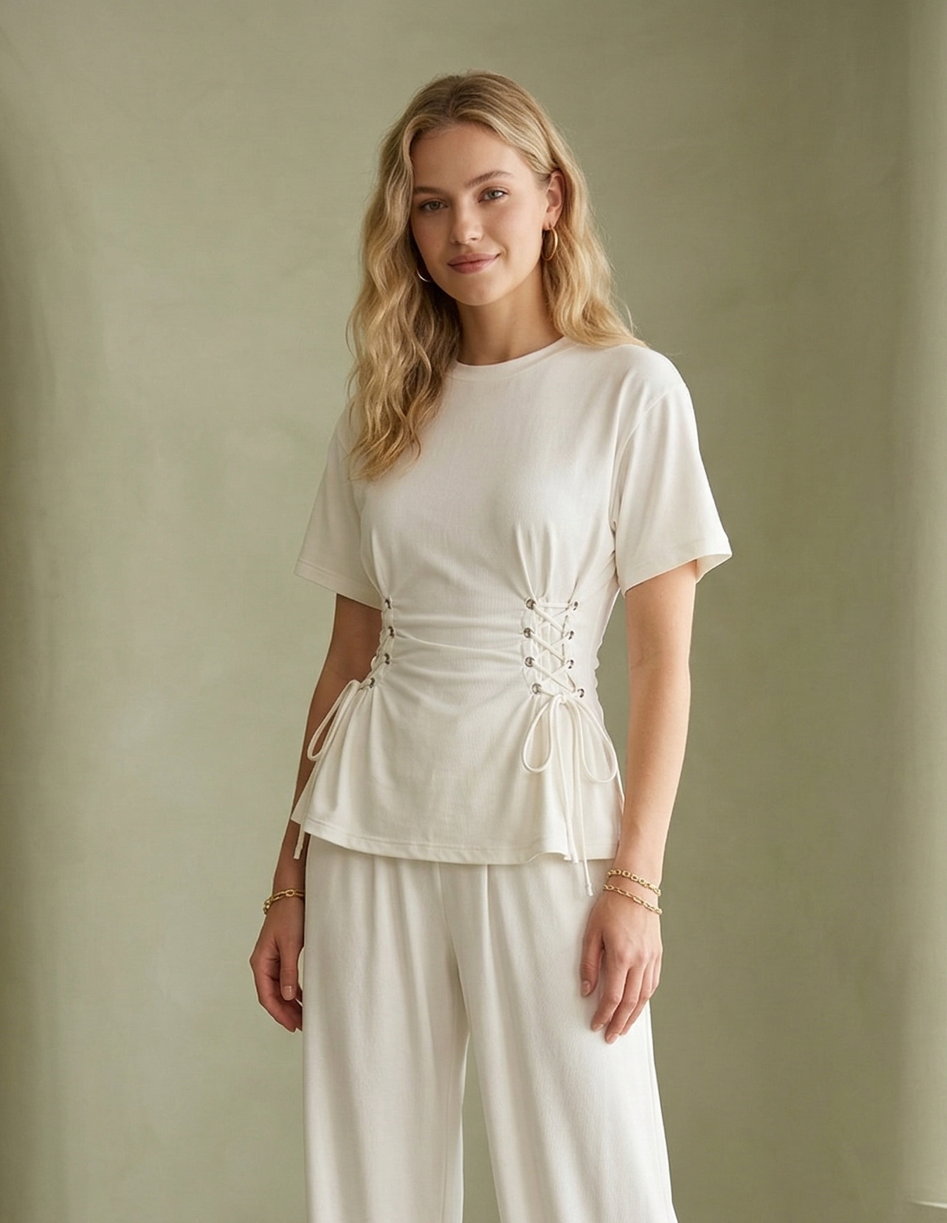 Woman wearing a white outfit standing against a plain wall.