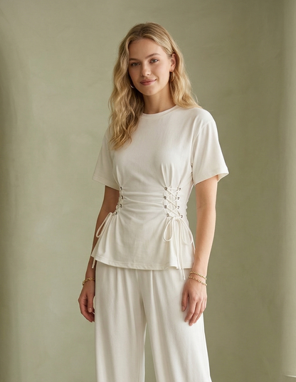 Woman wearing a white outfit standing against a plain wall.