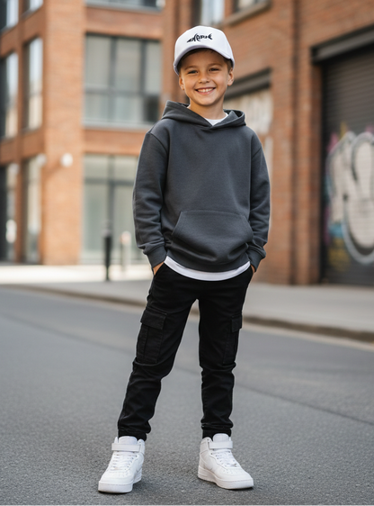 Child wearing a gray hoodie, black pants, and white sneakers standing on a street with graffiti in the background.