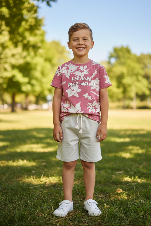 Child wearing a pink floral shirt and white shorts standing in a park.