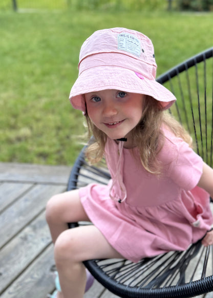 Young girl in a pink dress and hat sitting on a chair outdoors.