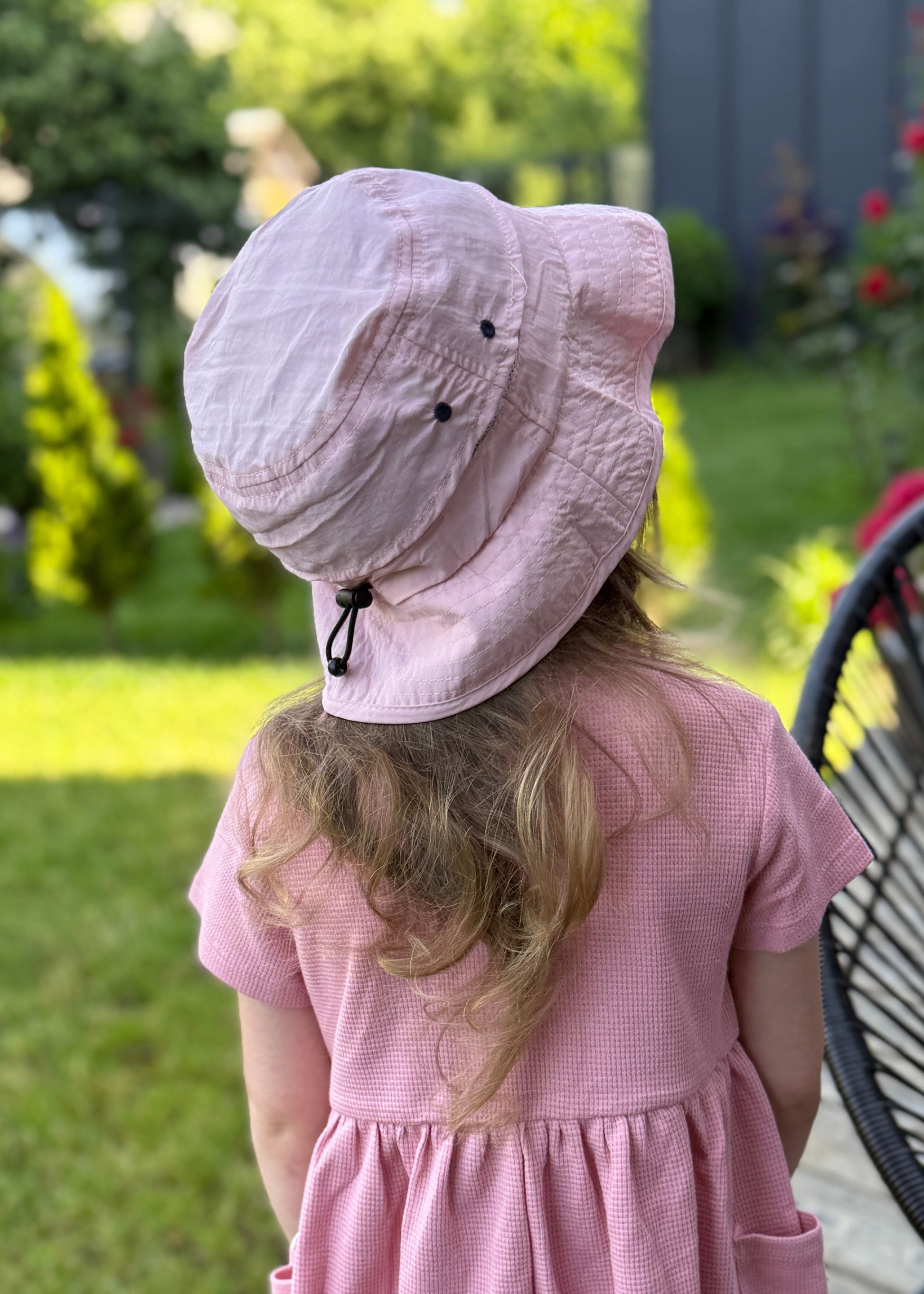 Child wearing a pink dress and sun hat in a garden setting