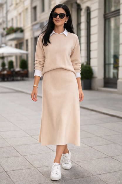 Woman wearing a beige sweater and skirt with white sneakers on a city street.