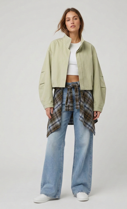 Woman wearing a light green jacket, white top, plaid shirt, and blue jeans on a white background