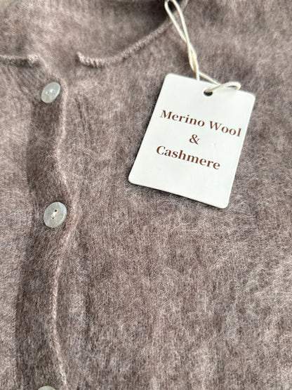 Close-up of a soft, fuzzy knit cardigan in a taupe-brown color, featuring a white paper tag that reads 'Merino Wool & Cashmere'.