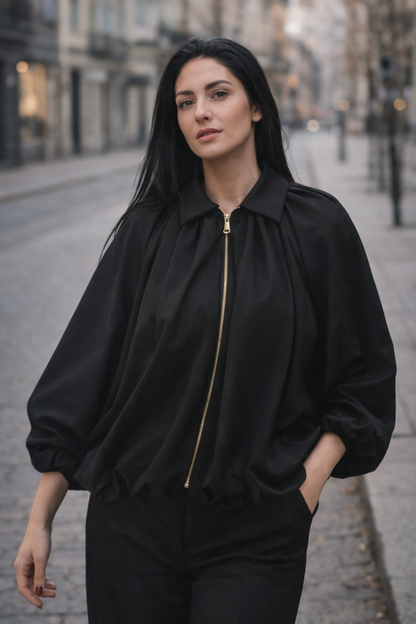 Woman wearing a black jacket with a gold zipper on a city street.