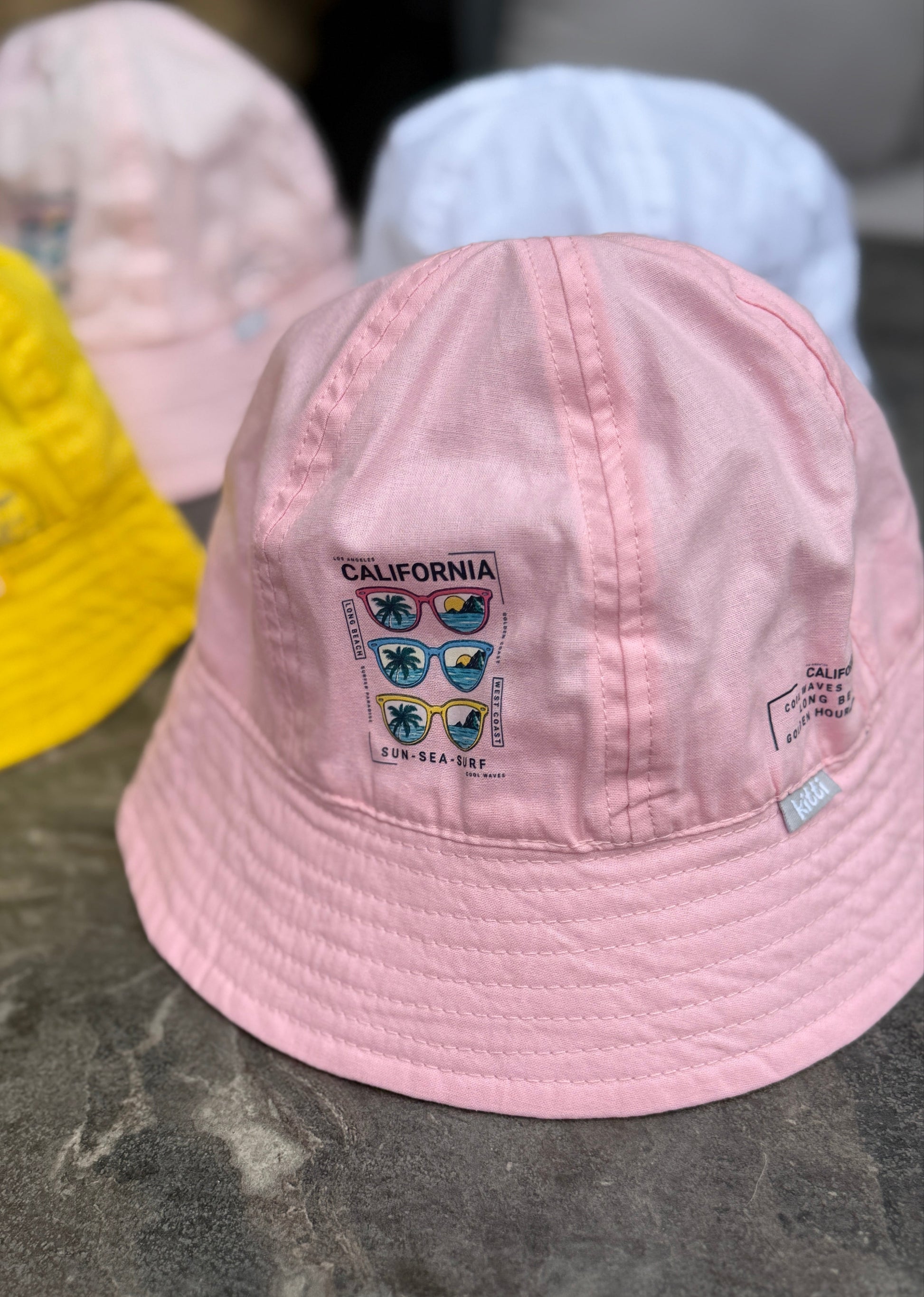 Pink bucket hat with 'California' and sunglasses design on a dark surface