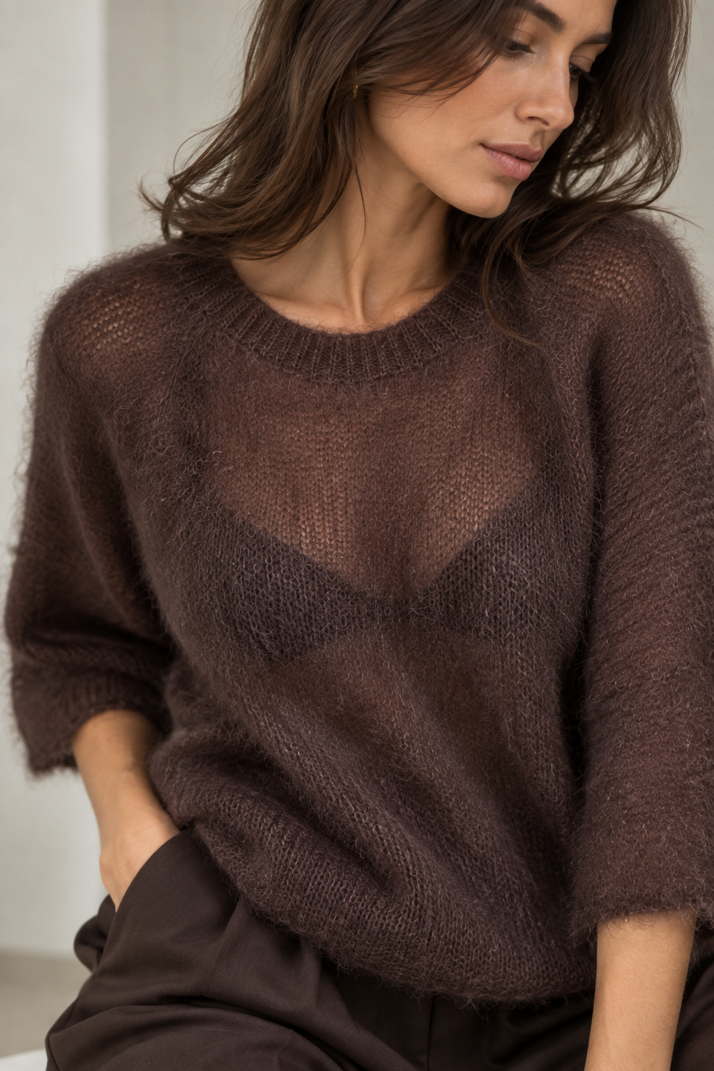 A woman wearing a fuzzy, open-knit brown sweater and dark brown trousers, shown in a close-up lifestyle shot.